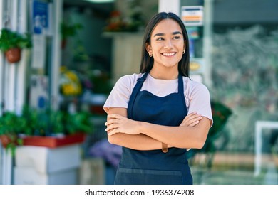 Young latin shopkeeper girl with arms crossed smiling happy standing at the florist