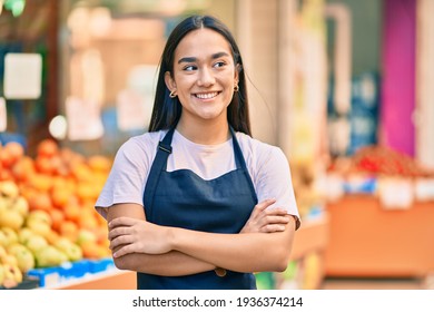 Young latin shopkeeper girl with arms crossed smiling happy at the fruit store.
