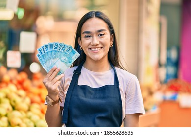 Young Latin Shopkeeper Girl Smiling Happy Holding Brazil Real Banknotes At The Fruit Store.