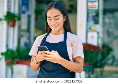 Young latin shopkeeper girl smiling happy using smartphone at florist. - Powered by Shutterstock