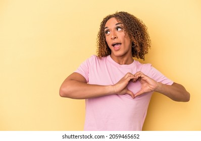 Young Latin Trans Woman Isolated On Yellow Background Smiling And Showing A Heart Shape With Hands.