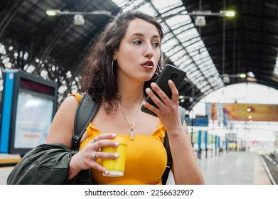 young latin woman of argentinian ethnicity, is worried at the train station stop sending a voice message on the phone, solving a problem with the trip. - Shutterstock ID 2256632907