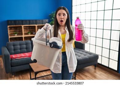 Young Latin Woman Cleaning The House Afraid And Shocked With Surprise And Amazed Expression, Fear And Excited Face. 