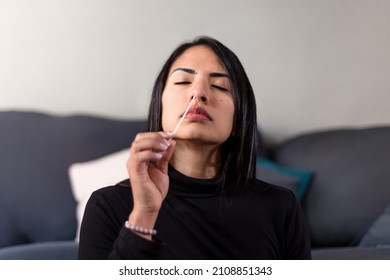 Young latin woman doing the auto test by inserting the swab into the nostril to prevent the coronavirus pandemic. Brunette woman at home doing the covid self-test.