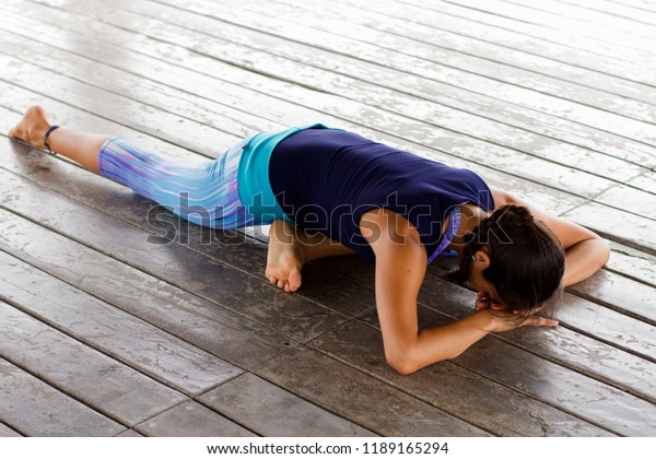 Young latin woman\
doing yoga relaxing pose. Resting on the floor. Pigeon yoga pose on\
a tropical beach area. 