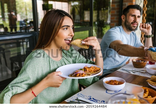 young latin\
woman eating mexican tacos on a restaurant terrace in Mexico Latin\
America, feeling happy on a summer\
day