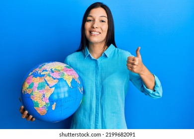 Young Latin Woman Holding Big World Ball Smiling Happy And Positive, Thumb Up Doing Excellent And Approval Sign 