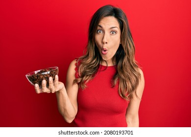Young latin woman holding bowl with raisins scared and amazed with open mouth for surprise, disbelief face 