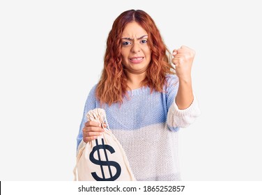 Young Latin Woman Holding Money Bag With Dollar Symbol Annoyed And Frustrated Shouting With Anger, Yelling Crazy With Anger And Hand Raised 