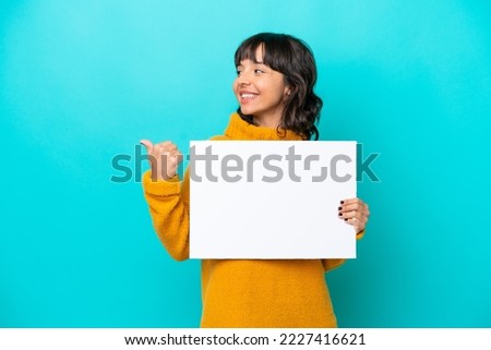 Young latin woman isolated on blue background holding an empty placard and pointing side
