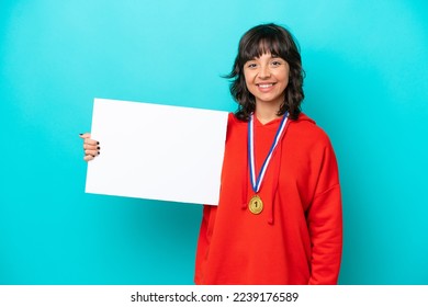 Young latin woman with medals isolated on blue background holding an empty placard with happy expression - Shutterstock ID 2239176589