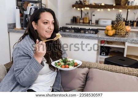 young latin woman overweight eating salad or healthy food at home in Mexico Latin America, hispanic plus size female in wellness concept
