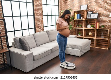 Young latin woman pregnant smiling confident measuring weight at home