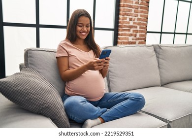 Young latin woman pregnant using smartphone at home - Powered by Shutterstock