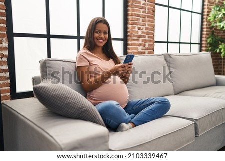 Young latin woman pregnant using smartphone at home