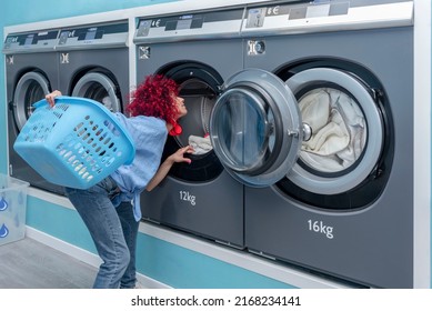 A Young Latin Woman With Red Afro Hair Looking For A Sock In An Industrial Washing Machine In A Blue Automatic Laundromat