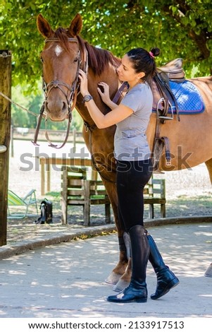 young latin woman rider caressing her horse in the field. vertical photo