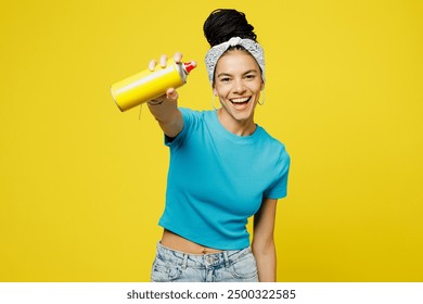 Young Latin woman she wears blue top t-shirt headband casual clothes hold paint spray bottle make graffiti stretch hand to camera isolated on plain yellow background studio portrait. Lifestyle concept - Powered by Shutterstock