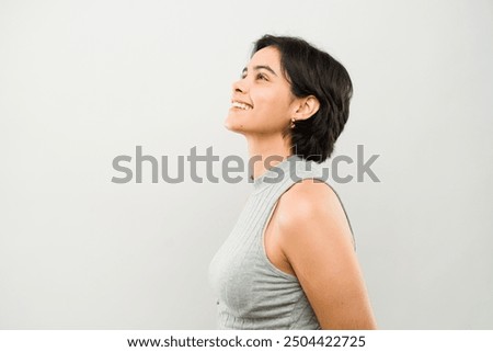 Young latin woman with short hair wearing a grey shirt smiling and looking up on a white background
