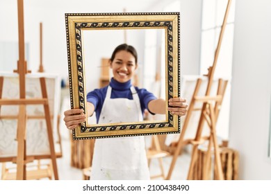 Young Latin Woman Smiling Confident Holding Empty Frame At Art Studio