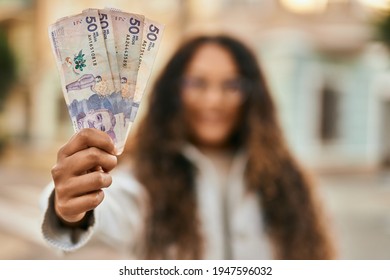 Young latin woman smiling happy holding colombia pesos banknotes at the city.