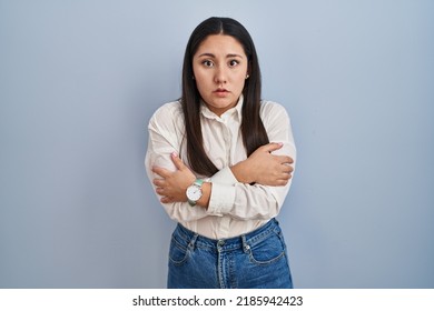 Young latin woman standing over blue background shaking and freezing for winter cold with sad and shock expression on face  - Shutterstock ID 2185942423