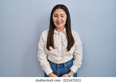 Young Latin Woman Standing Over Blue Background Winking Looking At The Camera With Sexy Expression, Cheerful And Happy Face. 