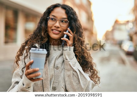 Young latin woman talking on the smartphone and drinking coffee at the city.