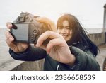young latin woman traveling through Buenos Aires, outdoors on a cloudy and cold day, taking a selfie photo with her digital DSRL camera, focus on the camera