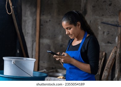 Young latin woman using a mobile phone while working in a rural kitchen - Powered by Shutterstock