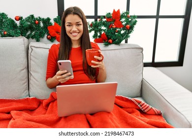 Young Latin Woman Using Smartphone Sitting By Christmas Decor At Home