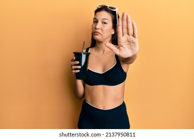 Young Latin Woman Wearing Bikini Drinking Soda With Open Hand Doing Stop Sign With Serious And Confident Expression, Defense Gesture 