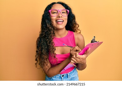 Young Latin Woman Wearing Business Clothes Writing On Clipboard Smiling And Laughing Hard Out Loud Because Funny Crazy Joke. 