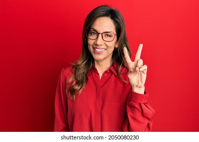 Young latin woman wearing casual clothes and glasses showing and pointing up with fingers number two while smiling confident and happy. 