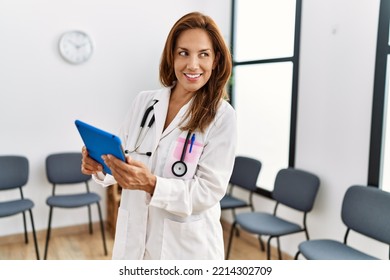 Young Latin Woman Wearing Doctor Uniform Using Touchpad At Clinic Waiting Room