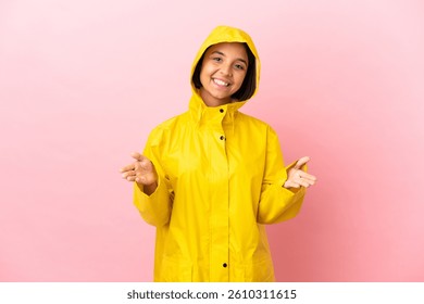Mujer latina joven que lleva un abrigo impermeable sobre fondo aislado que presenta e invita a venir con la mano