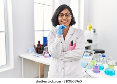 Mujer latina joven con uniforme científico de pie en el laboratorio