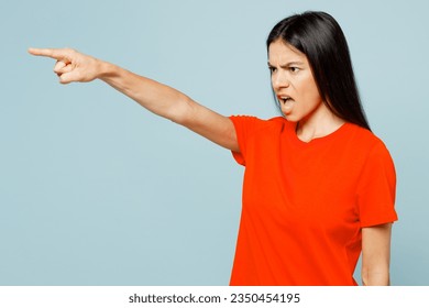 Young latin woman wears orange red t-shirt casual clothes point index aside on area scream shout command do it isolated on plain pastel light blue cyan background studio portrait. Lifestyle concept
