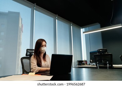 Young Latina Business Woman Wearing Covid-19 Protection Mask While Working On Her Laptop Inside The Office, Social Distancing And Work In Pandemic, Technology Concept