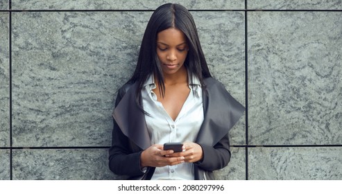 Young latina businesswoman portrait outdoors in Milan with modern building as background while using smart phone. 