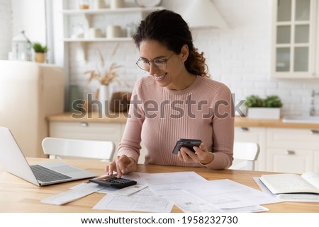 Young latina female work with financial papers at home count on calculator before paying taxes receipts online by phone. Millennial woman planning budget glad to find chance for economy saving money