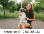 Young Latina with pug dog on a park swing in summer
