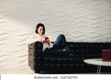 Young latina woman messaging with mobile telephone on sofa at home. Happy hispanic girl with cell phone. People using smartphone for texting message
