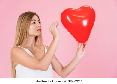 Young latina woman playing with a heart-shaped balloon. With a needle about to break the heart, valentine concept. Woman angry with love. Concept of revenge in love. 