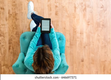 Young latina woman reading with an e-reader in a chair in a large interior room