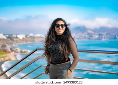 Young Latina woman smiling and enjoying the ocean view on a sunny day in Larcomar, Miraflores, Lima, Peru, with the coastline and mountains in the background. - Powered by Shutterstock