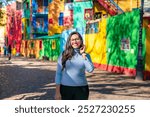 Young Latina woman smiling in front of the vibrant, colorful houses of Caminito, located in the La Boca neighborhood of Buenos Aires.