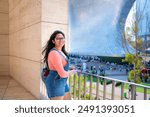 Young Latina woman smiling at Museo Jumex, with Soumaya Museum in the background, in Polanco, Mexico City.