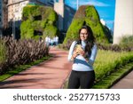 Young Latina woman smiling and using her phone near green sculptures in Buenos Aires, Argentina, enjoying a sunny day.