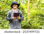 Young Latino biology student holding a tablet and smiling at the camera amidst Amazon rainforest trees